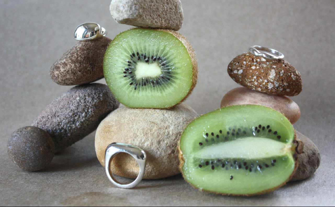 Kiwi fruits and stones with rings on a neutral background